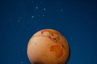 A globe with highlighted continents is positioned against a backdrop of a night sky filled with stars. The globe is tilted, displaying parts of the continents of Asia and Australia prominently. The night sky is a deep shade of blue, dotted with subtle white stars.