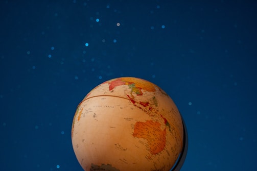 A globe with highlighted continents is positioned against a backdrop of a night sky filled with stars. The globe is tilted, displaying parts of the continents of Asia and Australia prominently. The night sky is a deep shade of blue, dotted with subtle white stars.