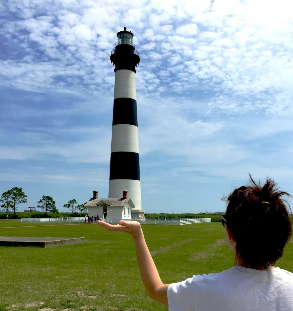 woman in white t-shirt holding black and white lighthouse under white clouds during daytime