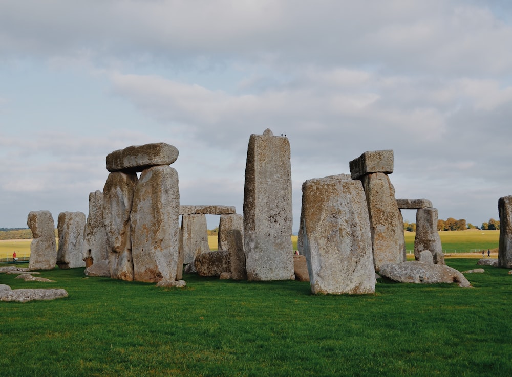 gray rock formation on green grass field under white clouds during daytime