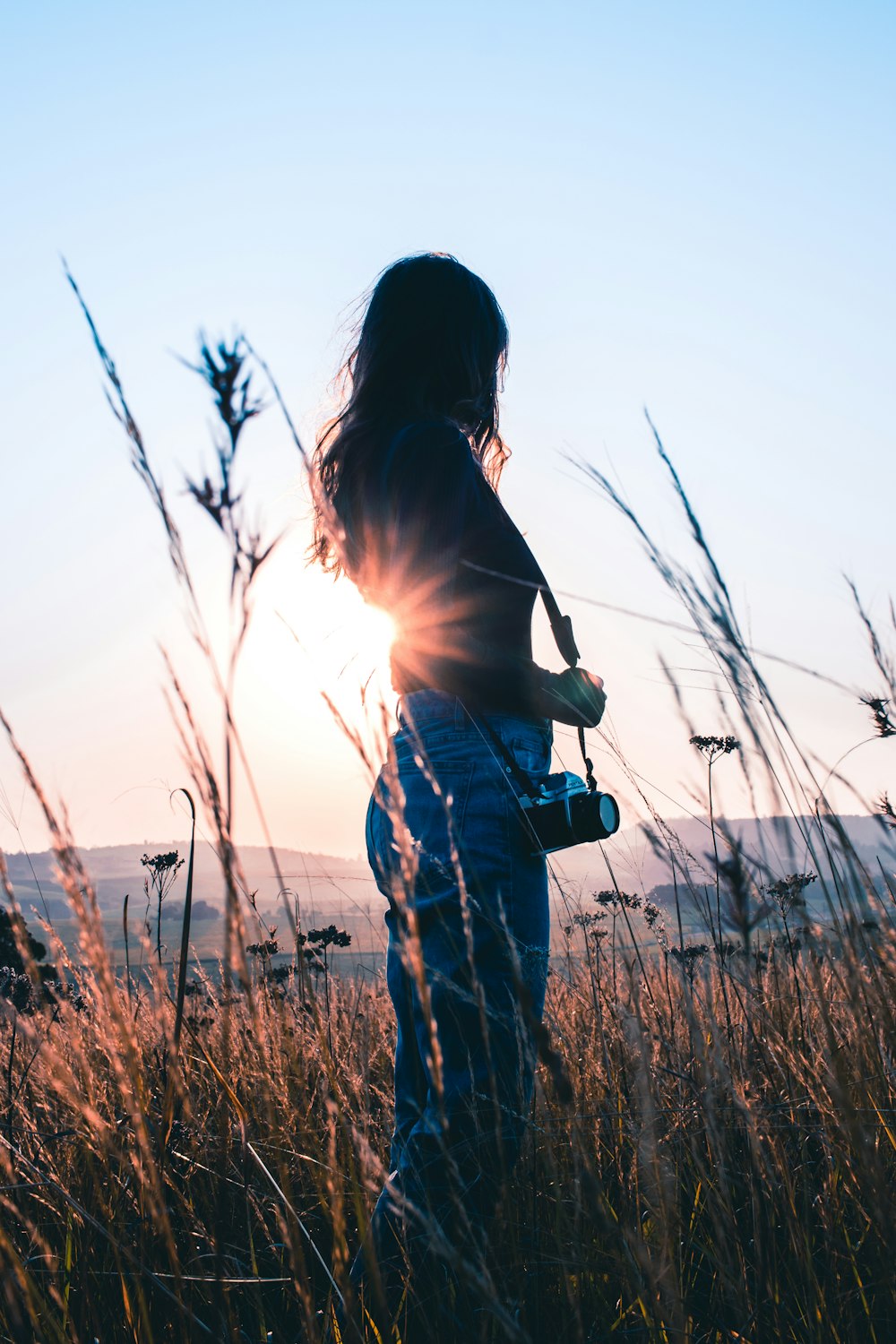 woman in brown tank top and blue denim jeans standing on green grass field during daytime