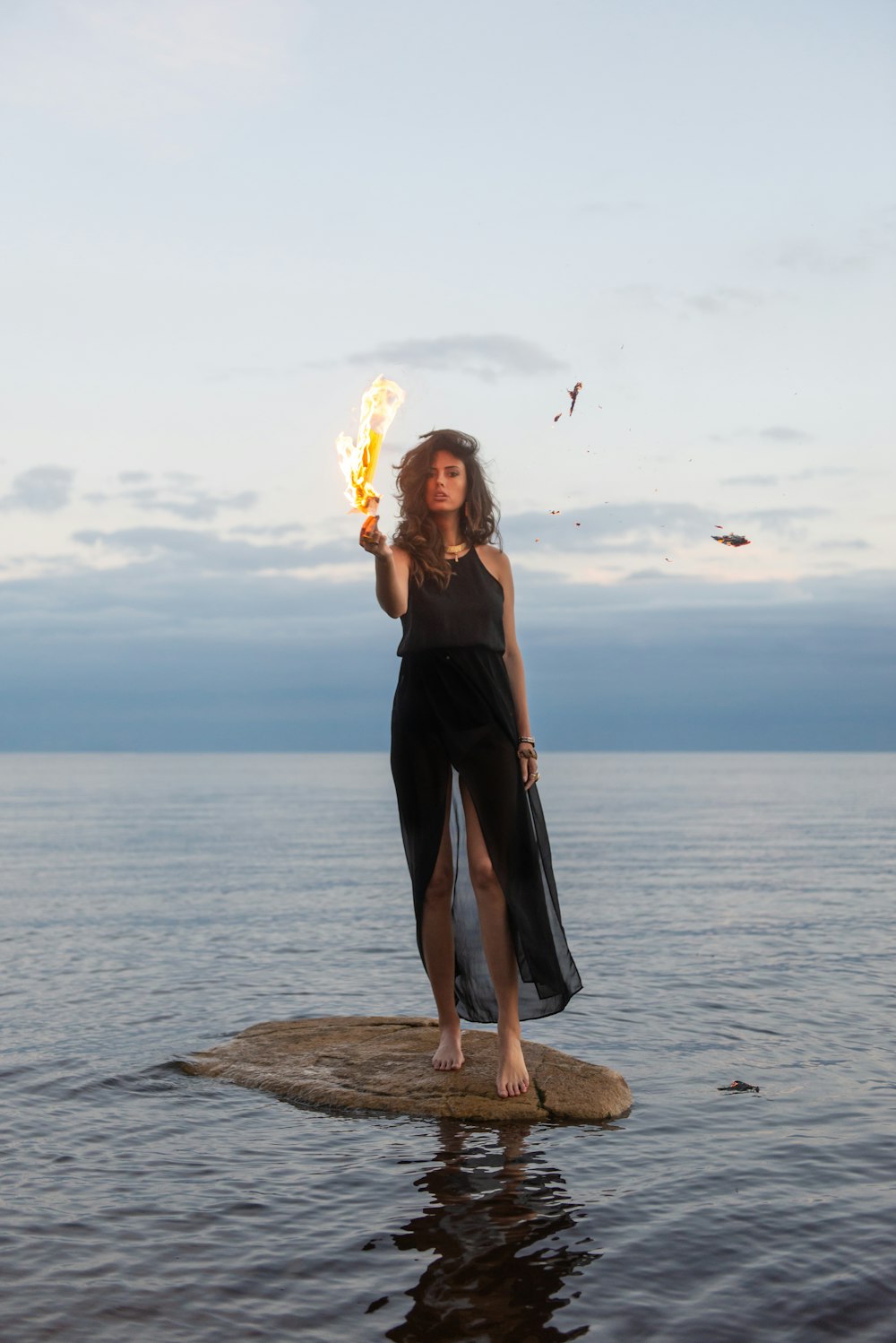 woman in black sleeveless dress standing on brown rock near sea during daytime