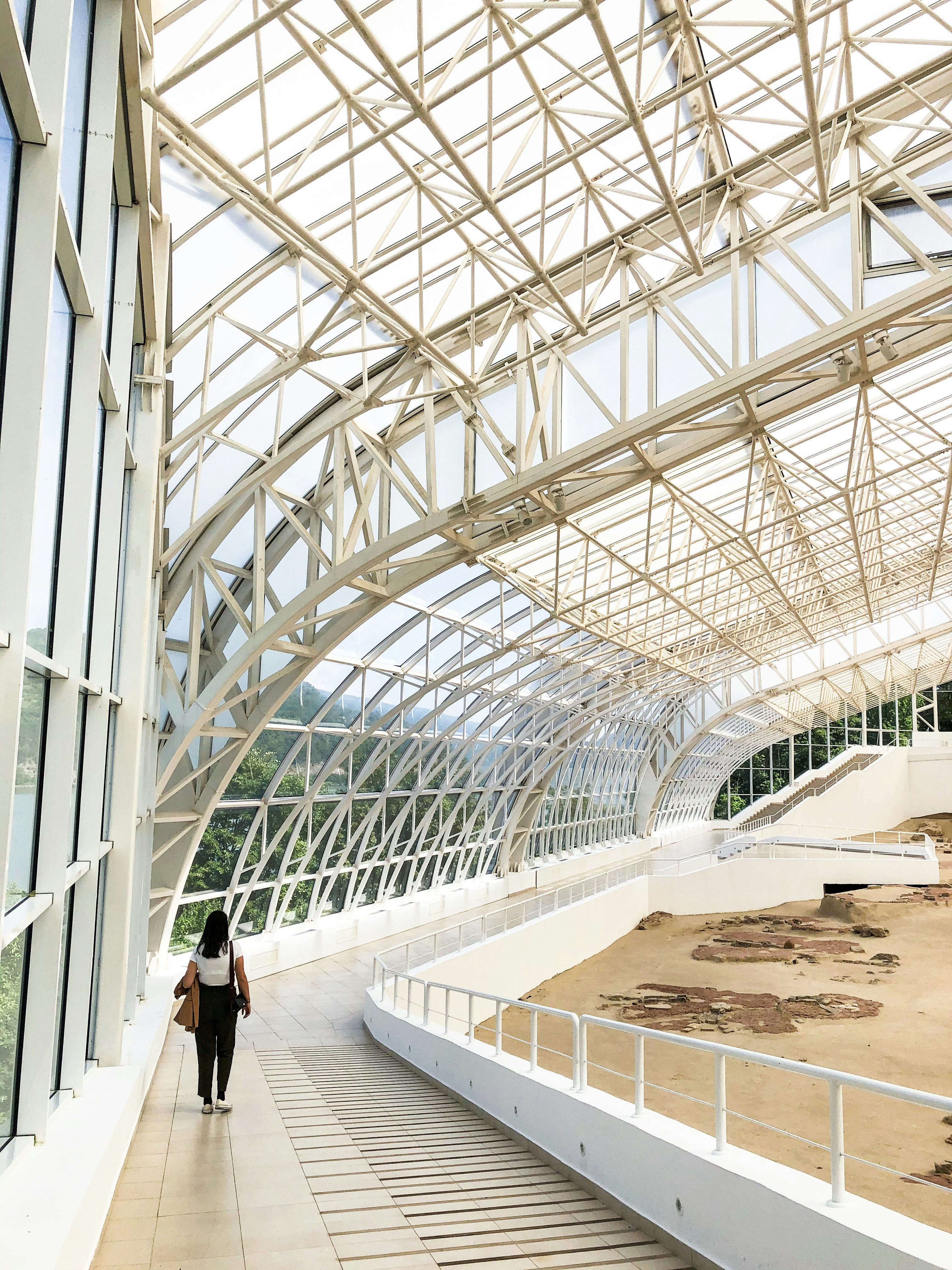 woman in black shirt walking on white concrete hallway
