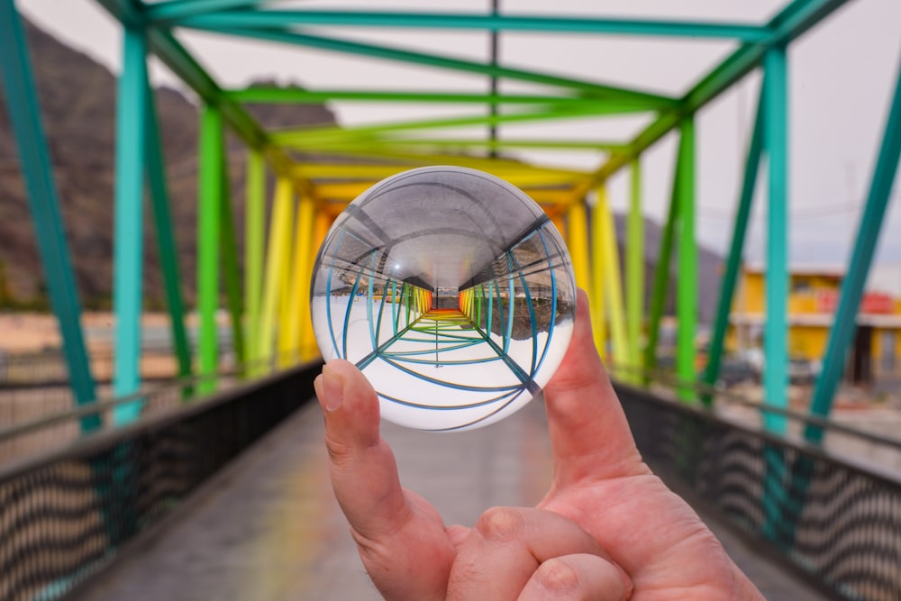 a hand holding a small glass ball in front of a bridge