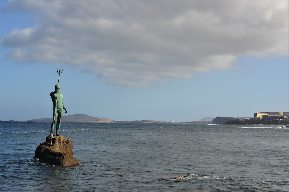 person in green shirt standing on brown rock formation near body of water during daytime