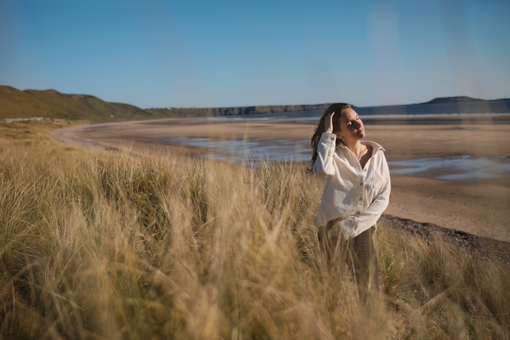 woman in white long sleeve shirt standing on green grass field near body of water during