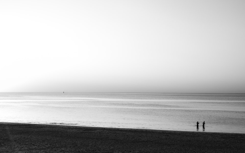 grayscale photo of person walking on beach