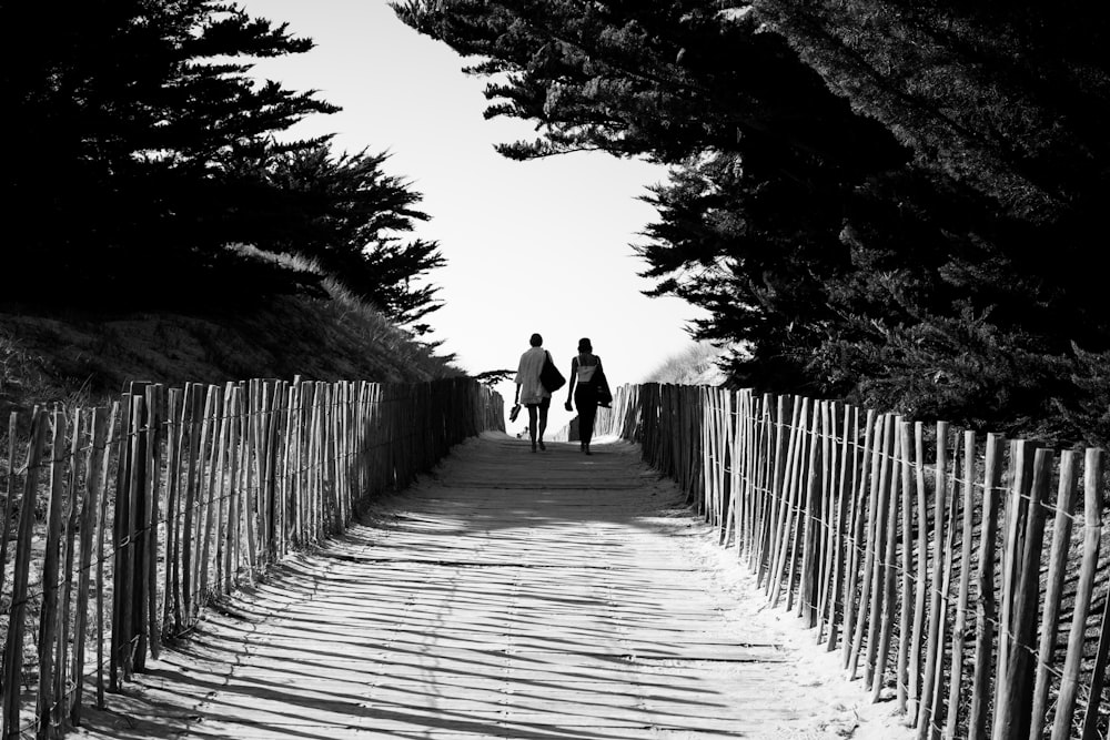 grayscale photo of 2 person walking on wooden pathway
