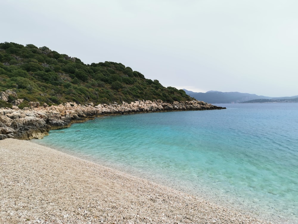 blue body of water near green and brown mountain under white clouds during daytime