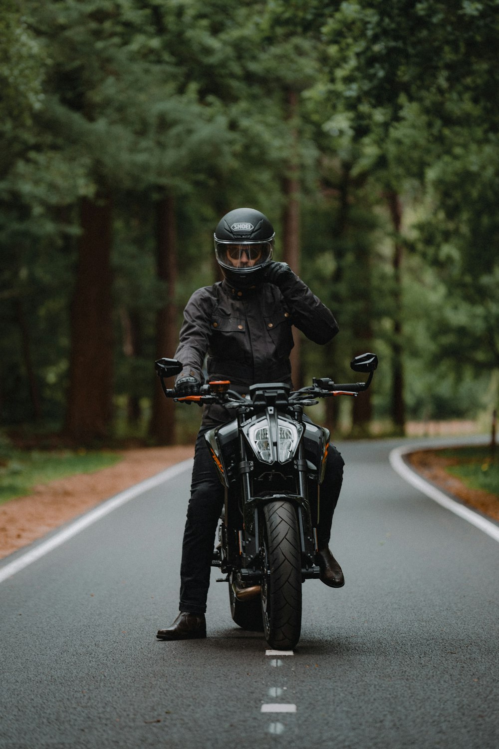 昼間の道路でバイクに乗る黒いジャケットの男