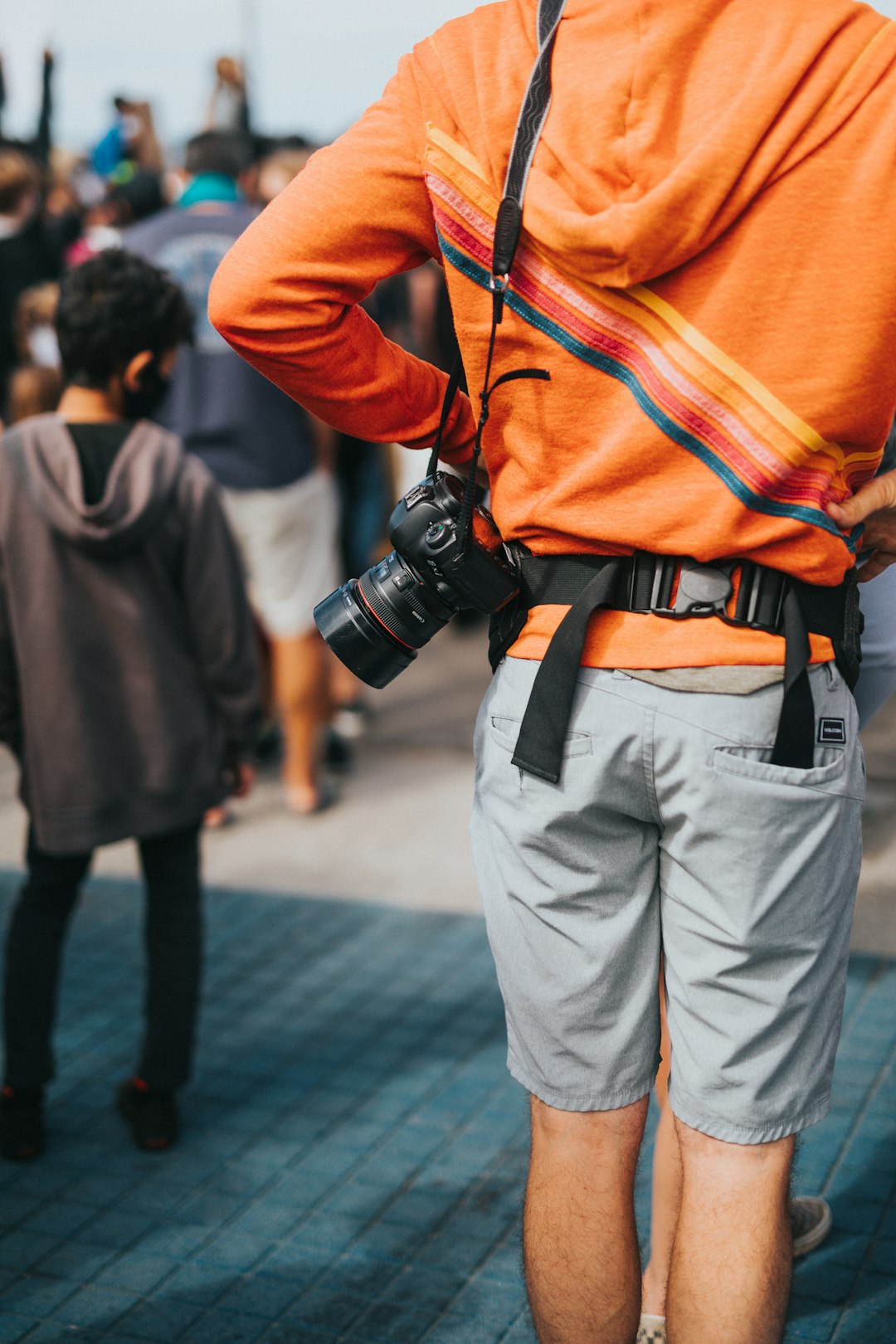 man in orange hoodie and gray pants with black dslr camera