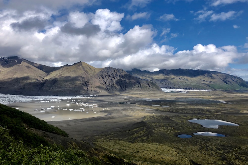 montanha verde e marrom sob nuvens brancas e céu azul durante o dia