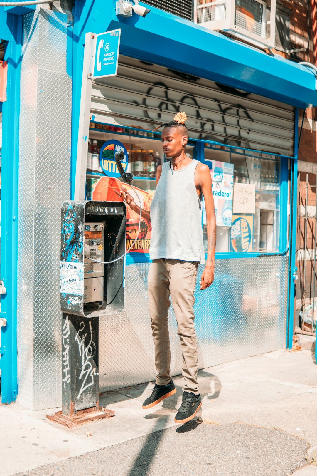 man in white tank top and beige pants standing beside blue metal fence during daytime