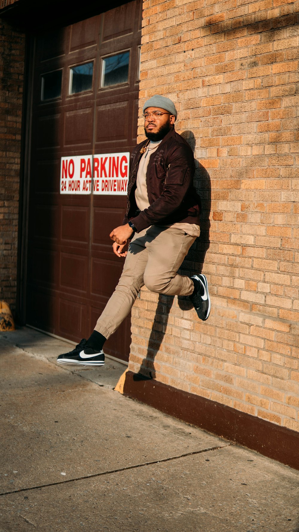 man in brown leather jacket and beige pants sitting on brown brick wall