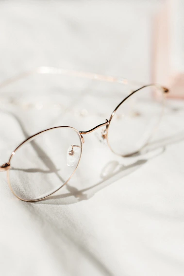 A close-up of stylish eyeglass frames resting on a light blue cloth, reflecting soft natural light.