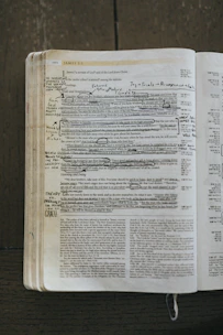 Close-up of hands open on an ancient Bible with notes and highlighters.