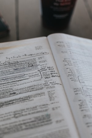 An open Bible with handwritten notes and underlined text. The pages are filled with annotations in pen, emphasizing certain passages. A blurred background suggests a cup is present on the table.