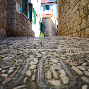 A charming medieval stone building with blue and white accents, nestled in a narrow cobblestone street of Gaeta at sunset.