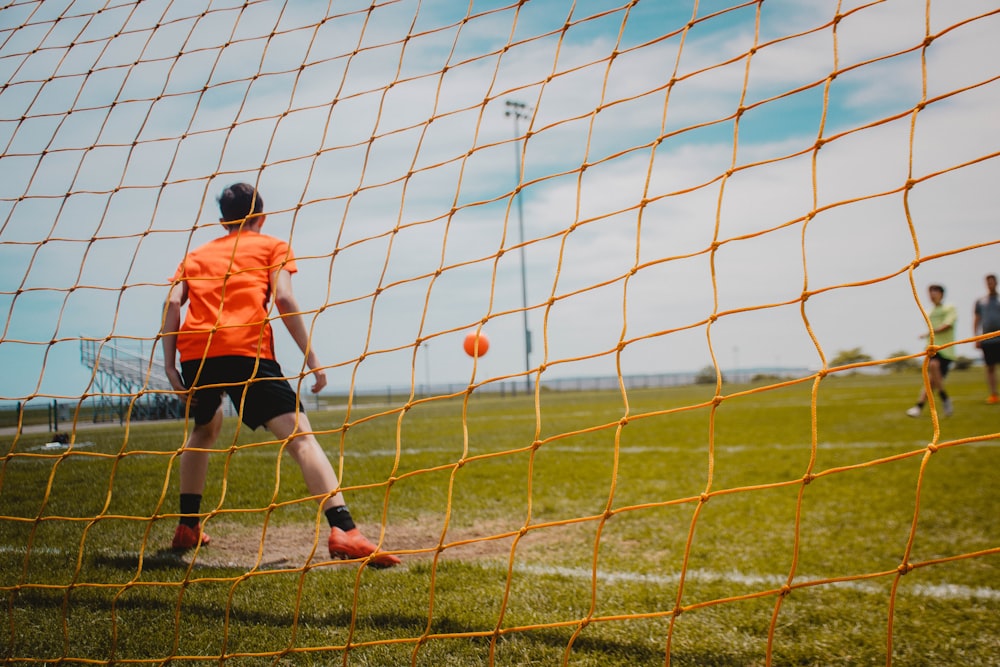 boy in orange shirt and black shorts playing soccer during daytime
