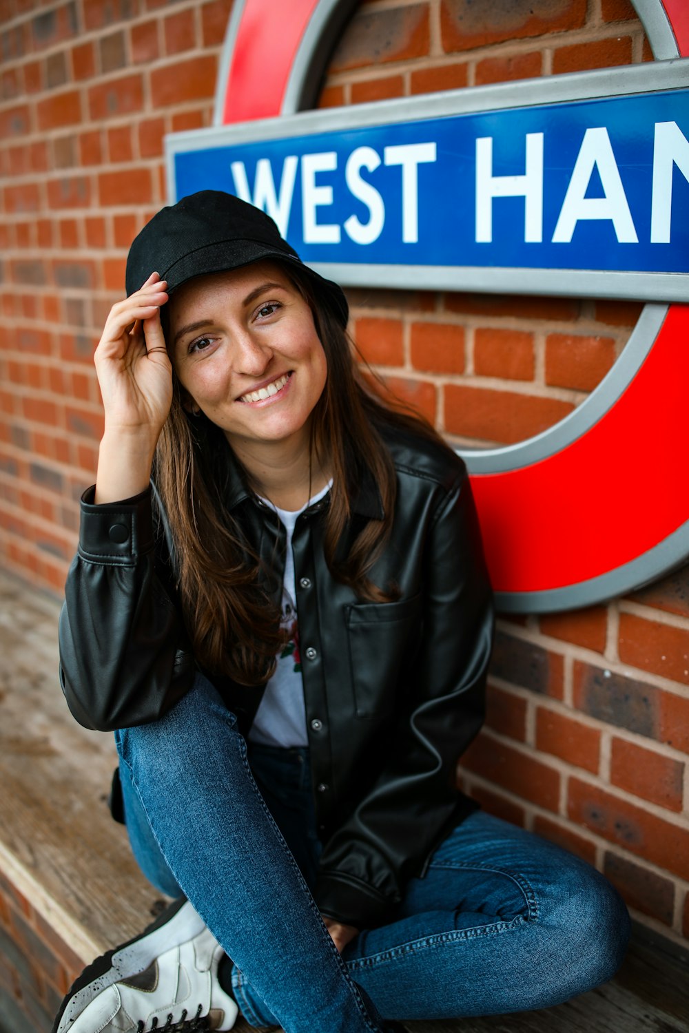 woman in black leather jacket and blue denim jeans sitting on brown concrete bench