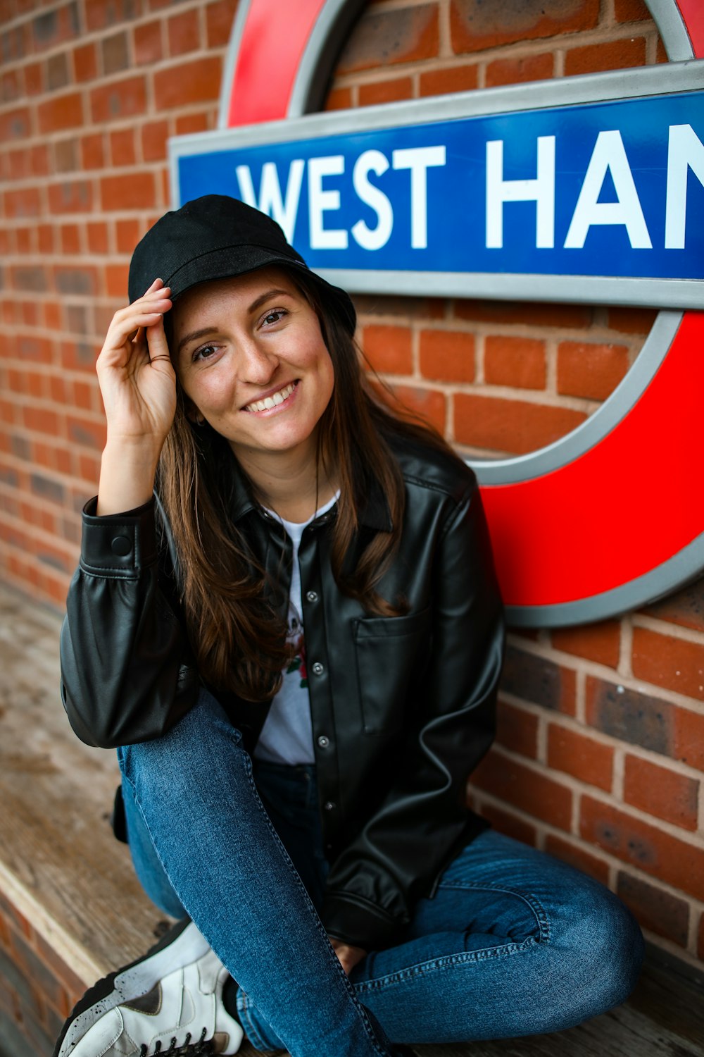 Frau in schwarzer Lederjacke und blauer Jeans sitzt auf brauner Betonbank