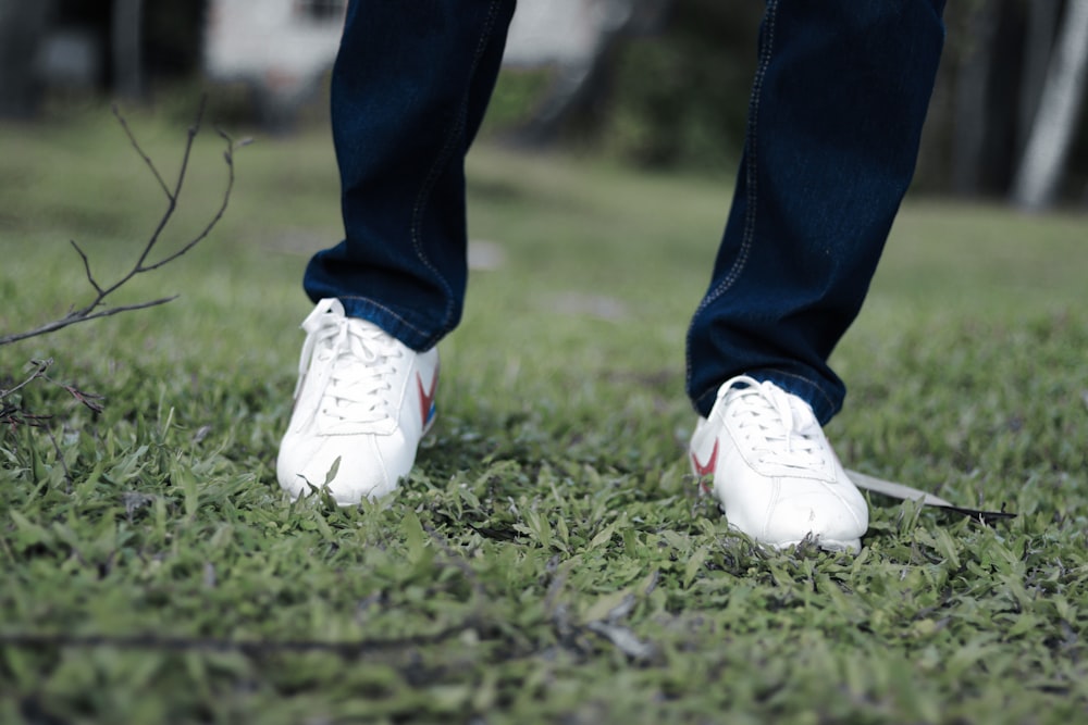 person in blue denim jeans and white nike sneakers standing on green grass field during daytime