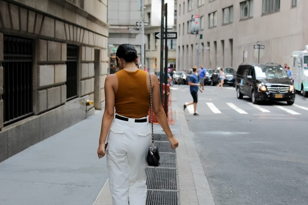 woman in orange shirt and white pants walking on sidewalk during daytime