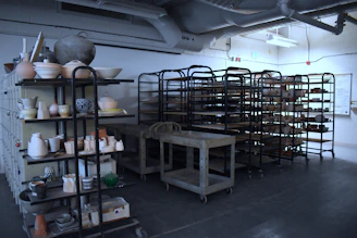 A bright, cozy studio workspace with colorful stoneware pieces drying on wooden shelves.