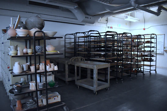 A bright, cozy studio workspace with colorful stoneware pieces drying on wooden shelves.