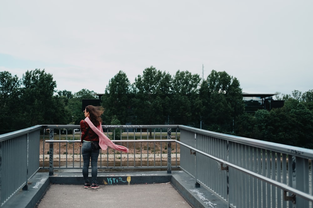 woman in red shirt and blue denim jeans walking on gray concrete bridge during daytime