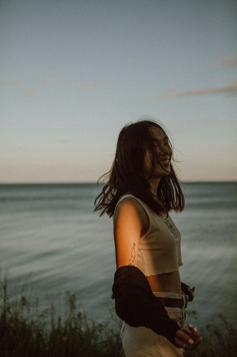 woman in white tank top standing near body of water during daytime