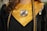 A close-up of a graduation gown with a gold stole that has an emblem at the center. Two colored cords, one blue and one gold, are draped over the gown. The gown also features a patch on the right side.