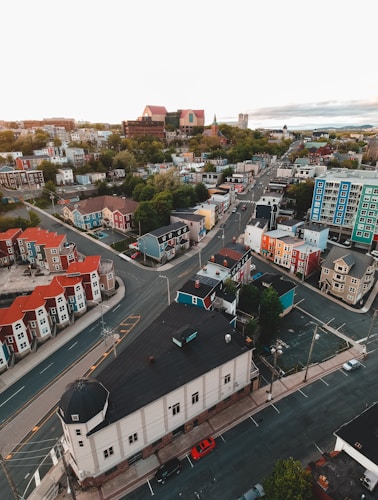 Aerial view of a colorful urban neighborhood featuring various multi-story buildings and houses. The buildings are painted in bright colors such as red, blue, and yellow, and are situated along a grid-like pattern of streets. Trees and greenery are interspersed among the buildings, indicating a mix of urban and natural elements. The sky is overcast, providing a subdued light to the scene.
