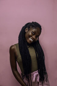 A smiling woman showcasing a sleek braided updo with soft pink highlights in natural light.
