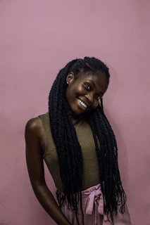 A smiling woman showcasing a sleek braided updo with soft pink highlights in natural light.