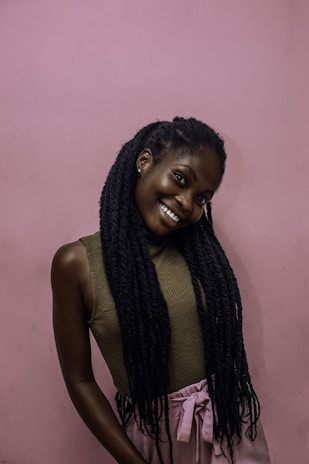 A warm pastel pink background with a smiling person sharing their story on video.