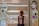 A woman is standing in front of a cosmetics display in a store, selecting a product. The shelves are filled with various foundation compacts, powders, and other beauty products. Advertisements and promotional images featuring models are visible on the surrounding walls.