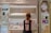 A woman is standing in front of a cosmetics display in a store, selecting a product. The shelves are filled with various foundation compacts, powders, and other beauty products. Advertisements and promotional images featuring models are visible on the surrounding walls.