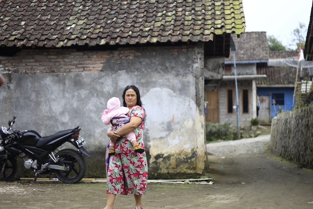 woman in pink and blue floral dress standing beside black motorcycle during daytime