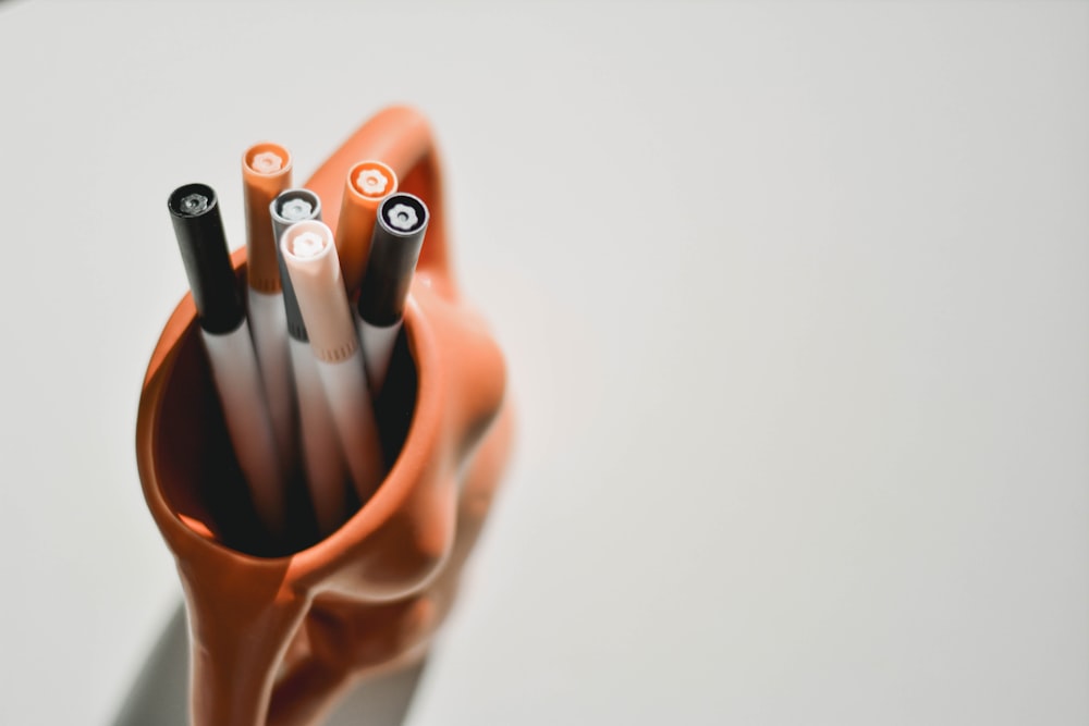 person holding black pen in brown ceramic mug