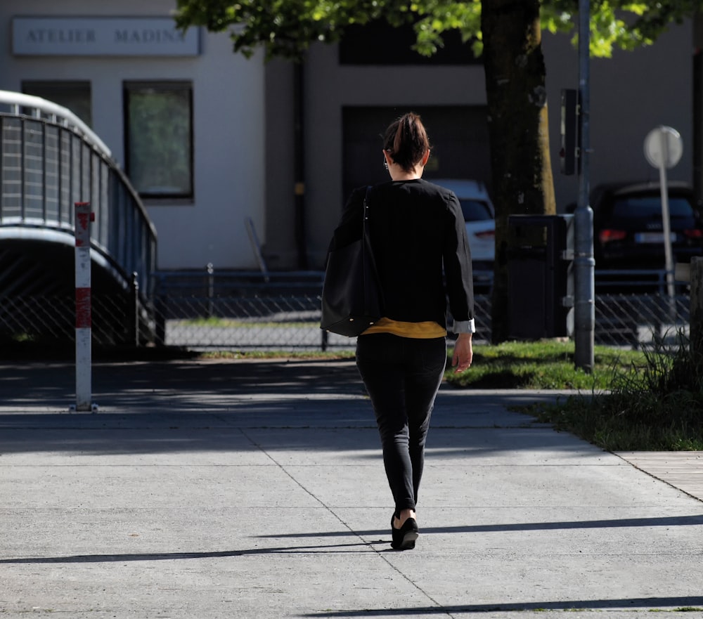 woman in black jacket and black pants walking on sidewalk during daytime