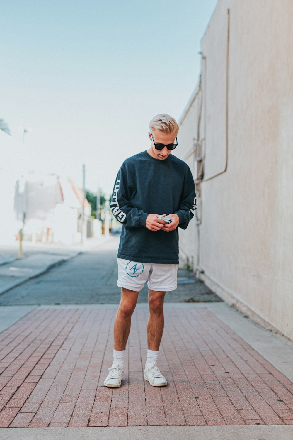 man in black long sleeve shirt and brown shorts standing on sidewalk during daytime