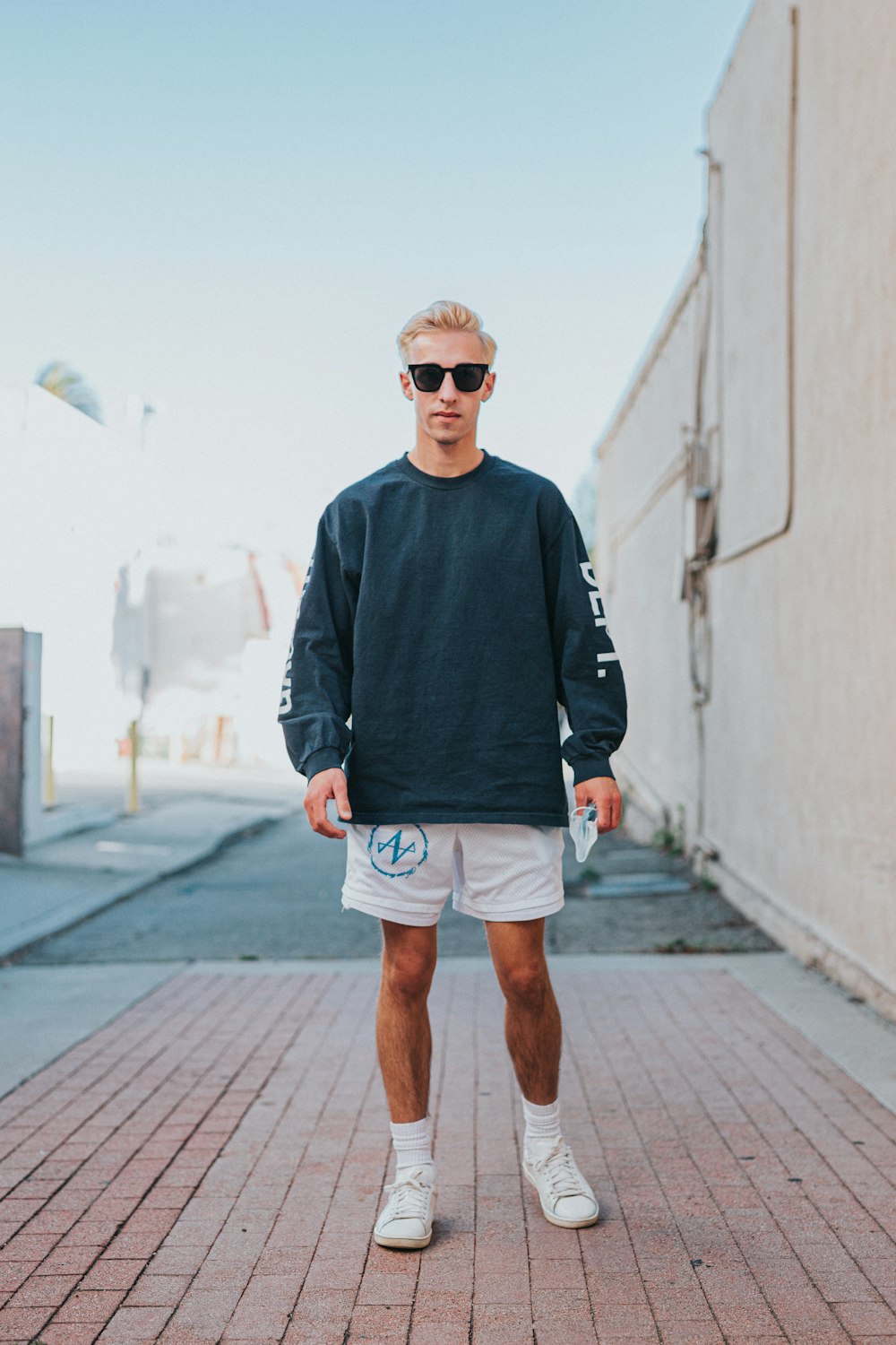 man in black sweater and white shorts standing on sidewalk during daytime