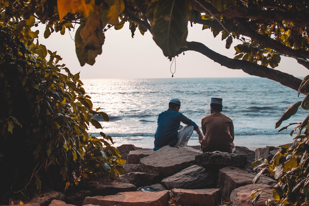 man sitting on rock near body of water during daytime