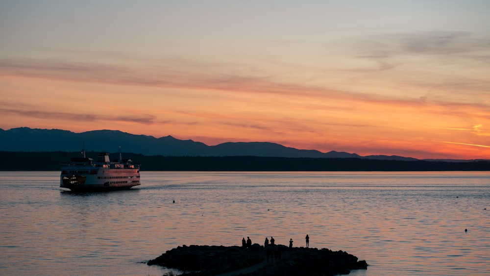 silhouette of people standing on rock formation near body of water during sunset