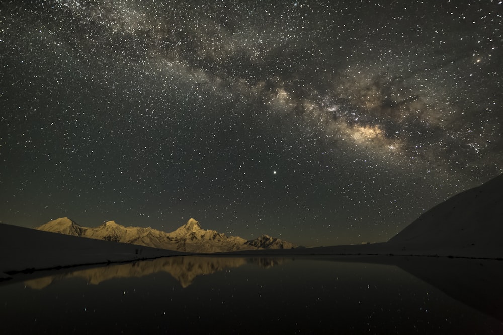 body of water near mountain under starry night