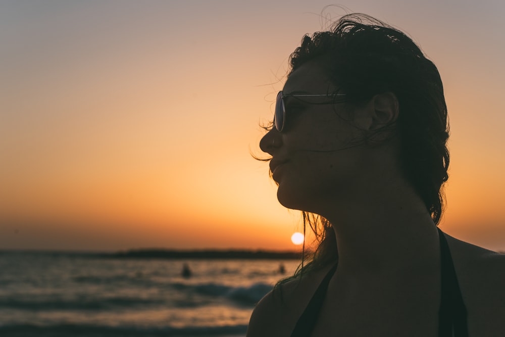 woman in brown jacket standing on beach during sunset