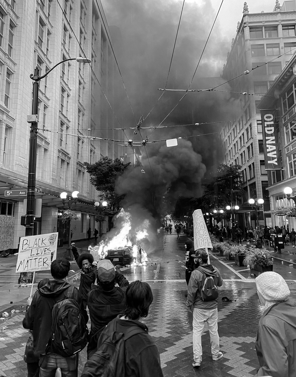 grayscale photo of people walking on street with smoke