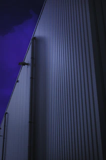An evening 4K shot of a metal sheet shed with blue roofing and steel frame, with warm light glowing inside, located in an Indian industrial area.