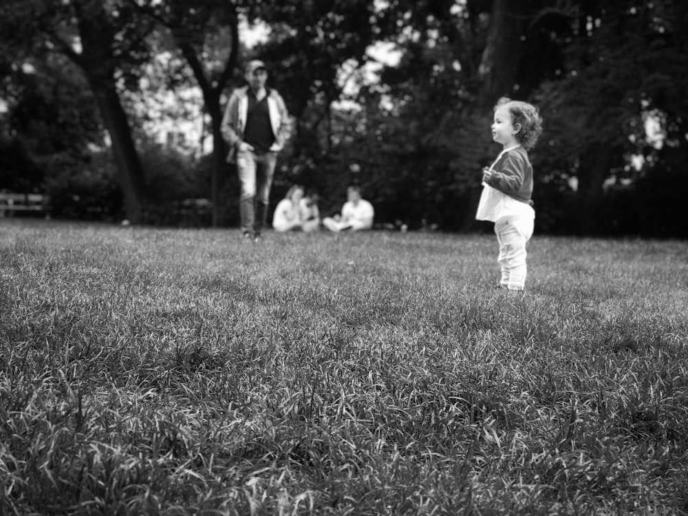 grayscale photo of boy in long sleeve shirt walking on grass field